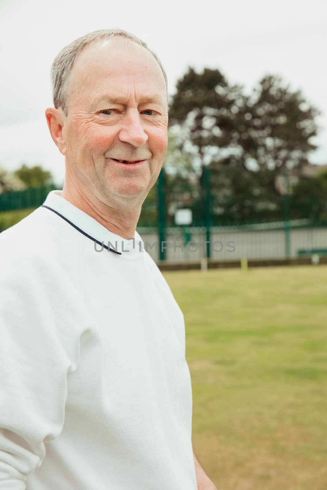 A portrait of a senior man smiling at a bowling green.