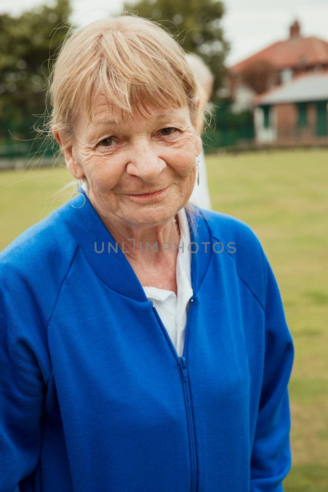 A portrait of a senior woman smiling at a bowling green.