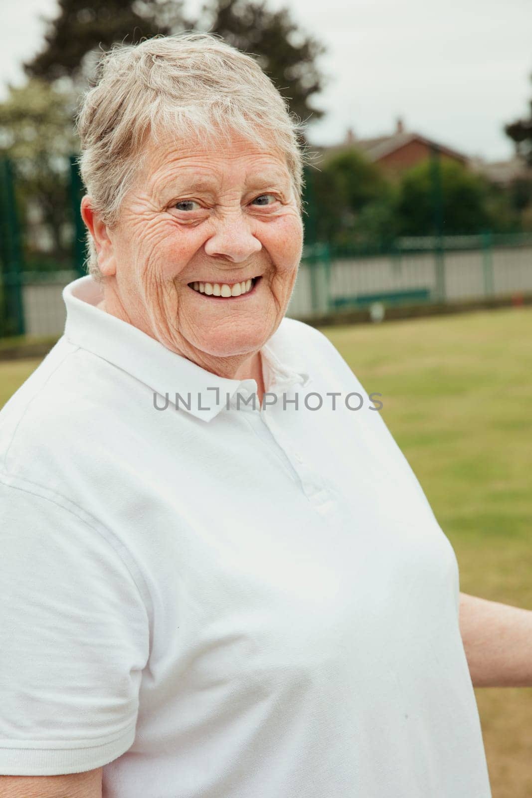 A portrait of a senior woman smiling at a bowling green.