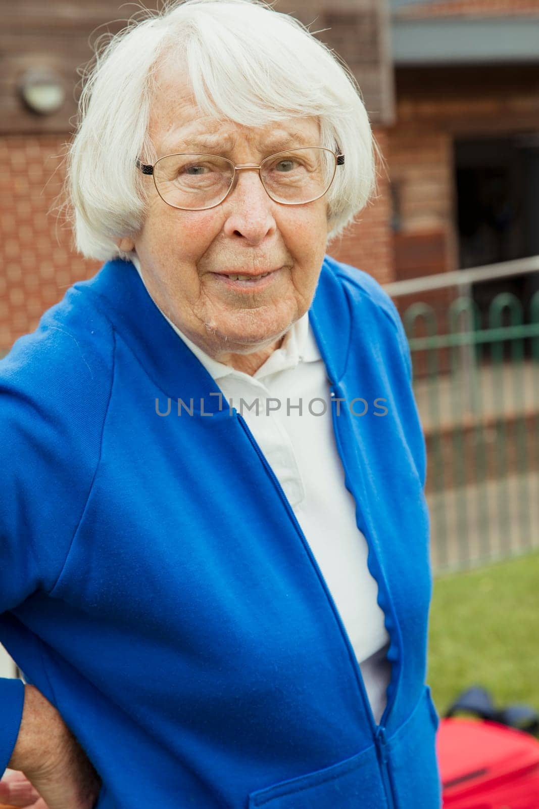 A portrait of a senior woman smiling at a bowling green. She is wearing glasses.