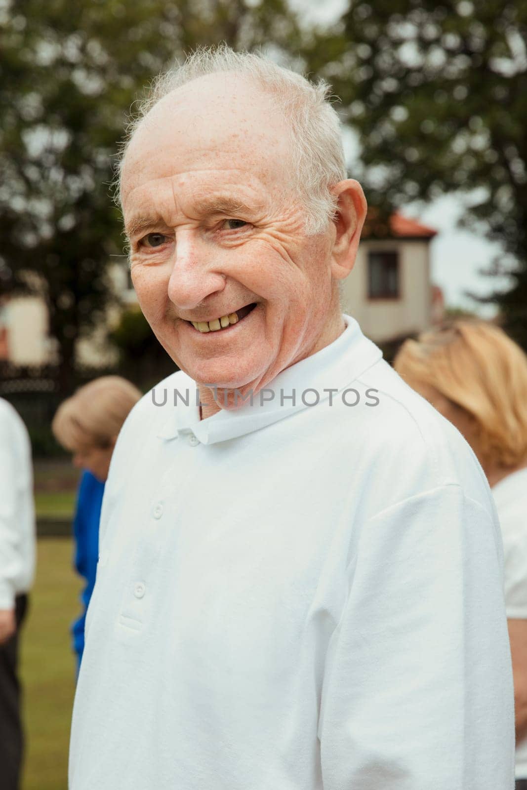 A portrait of a senior man smiling at a bowling green.