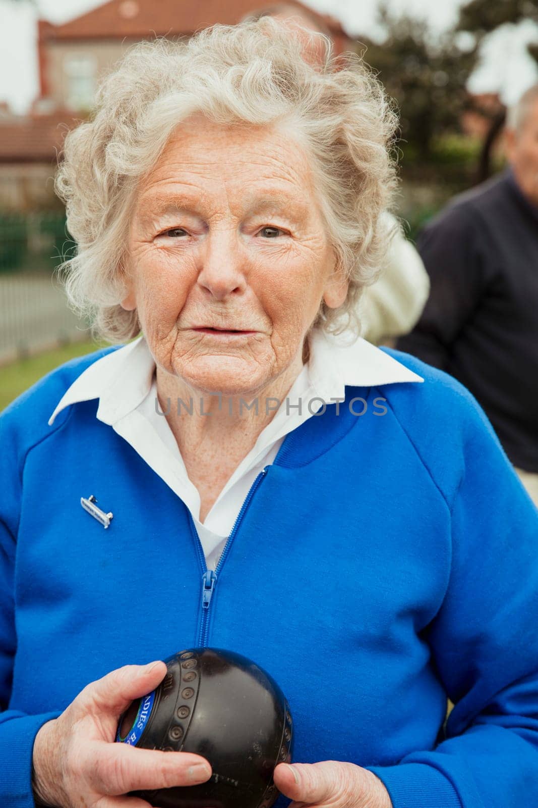 A portrait of a senior woman at a bowling green, holdng a bocce ball.