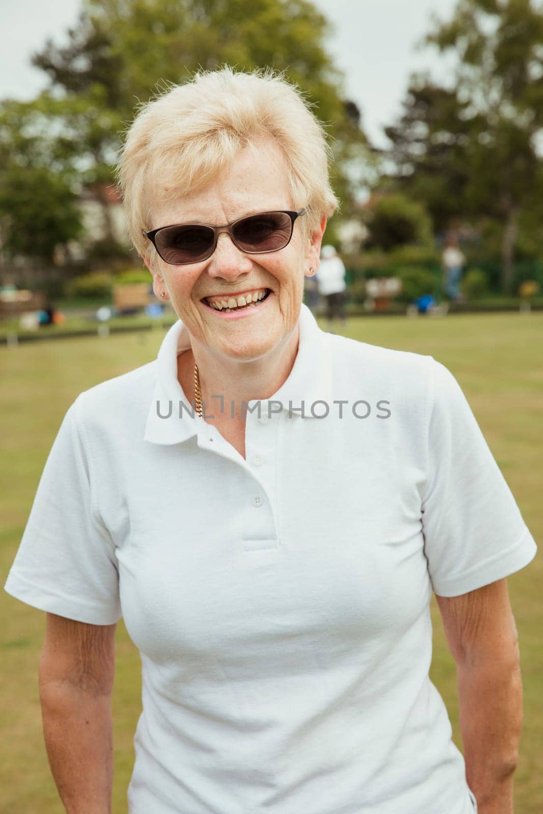 A portrait of a senior woman smiling at a bowling green.
