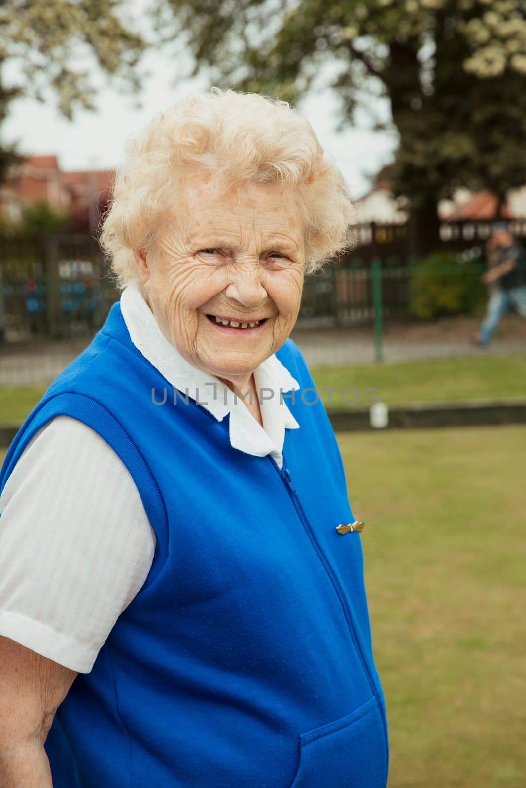 A portrait of a senior woman smiling at a bowling green.