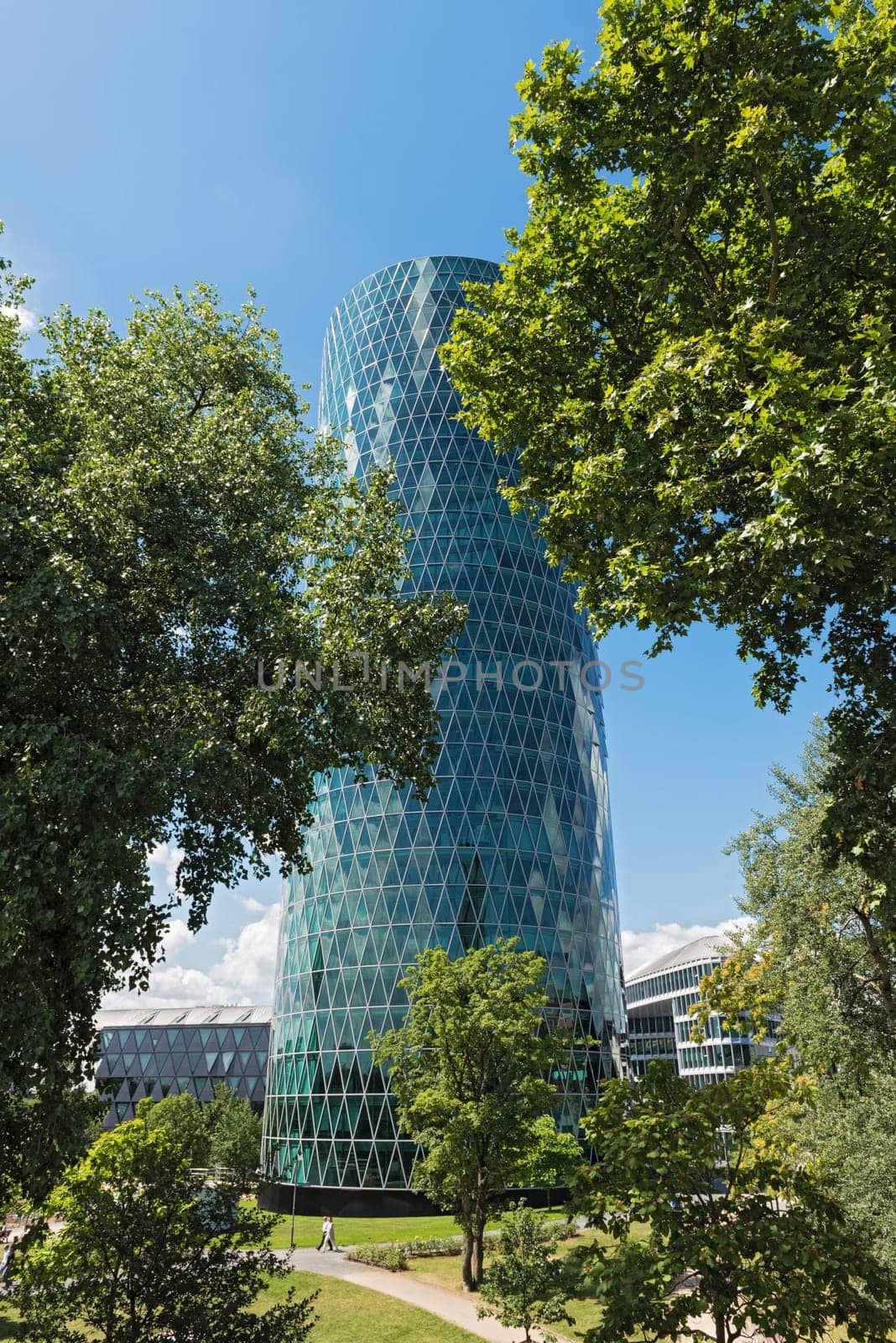 westhafen tower in frankfurt am main with trees in the front on a cloudy day
