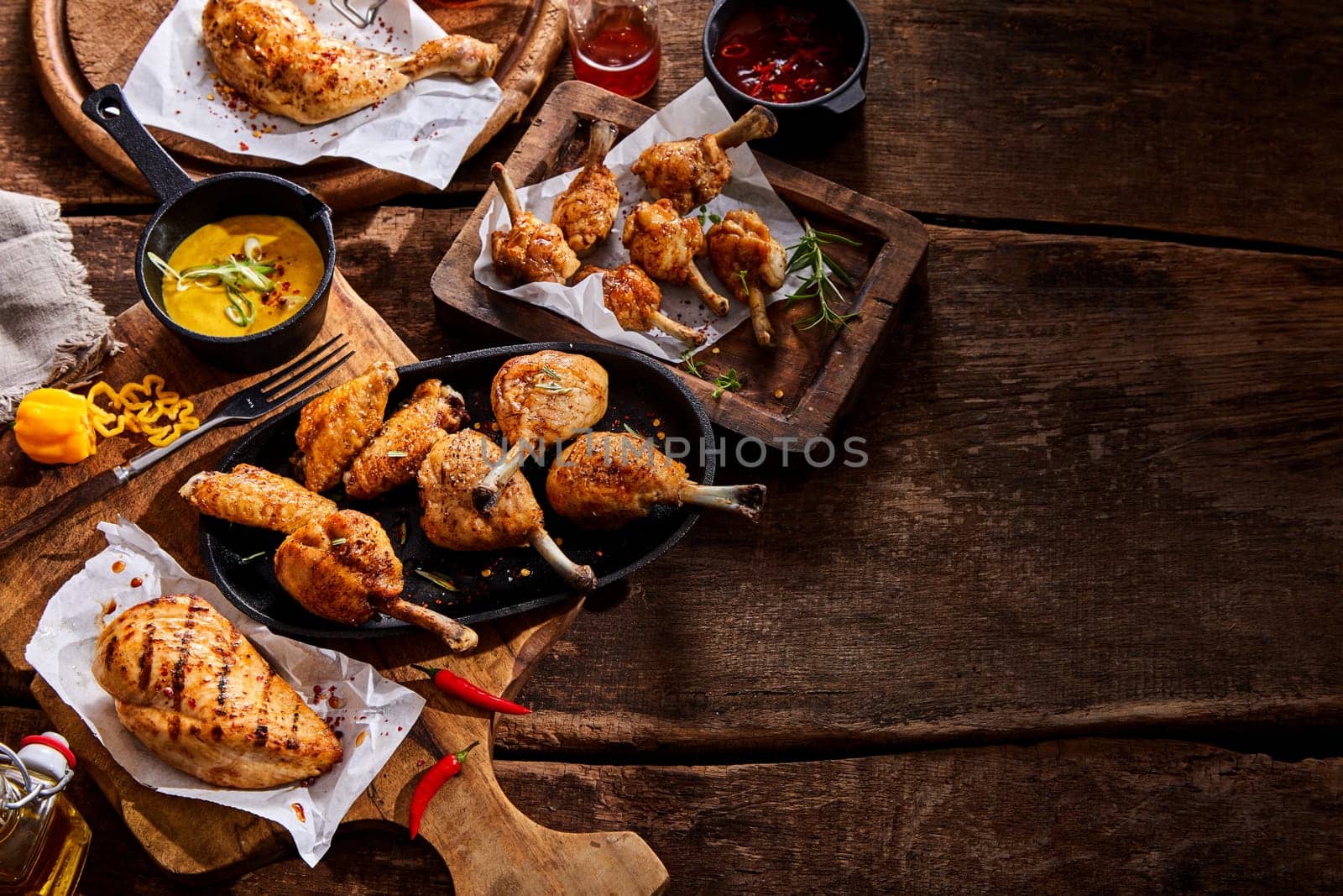 Assorted grilled chicken portions on a buffet table at a summer BBQ seasoned with hot chili pepper and fresh herbs and served with mustard dip, top down with copy space