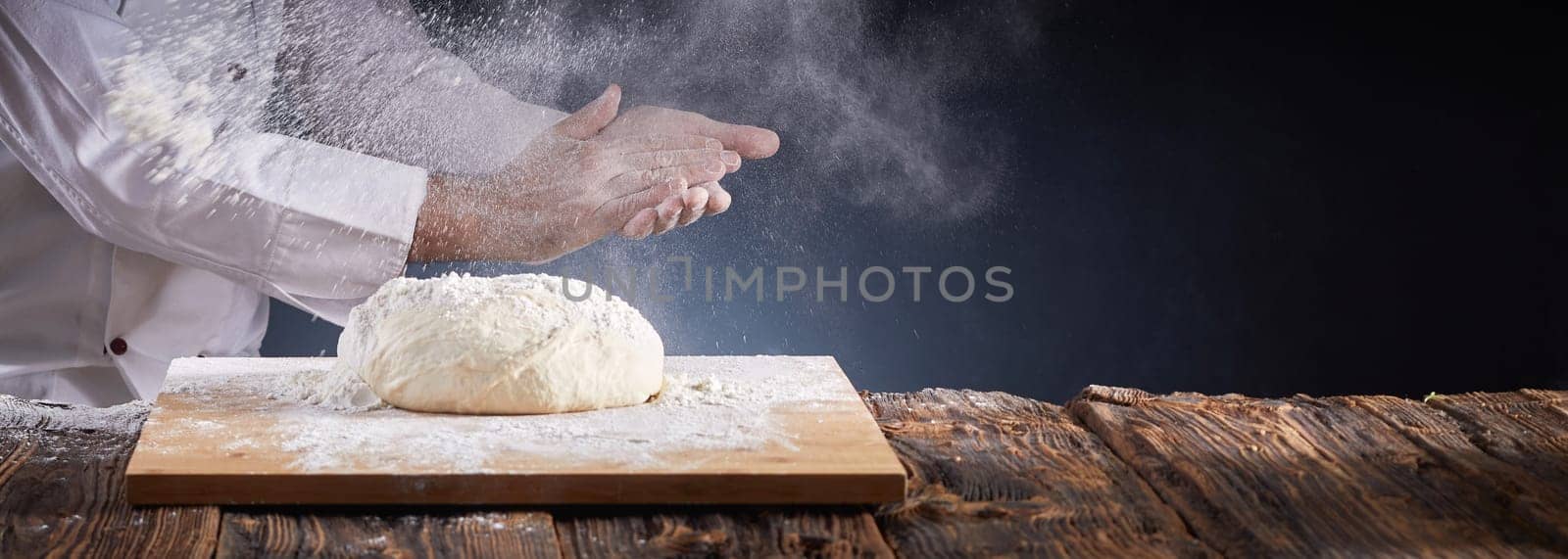 Chef or baker dusting a heap of uncooked dough with flour suspended in the air by clapping his hands in a rustic panorama banner with copy space