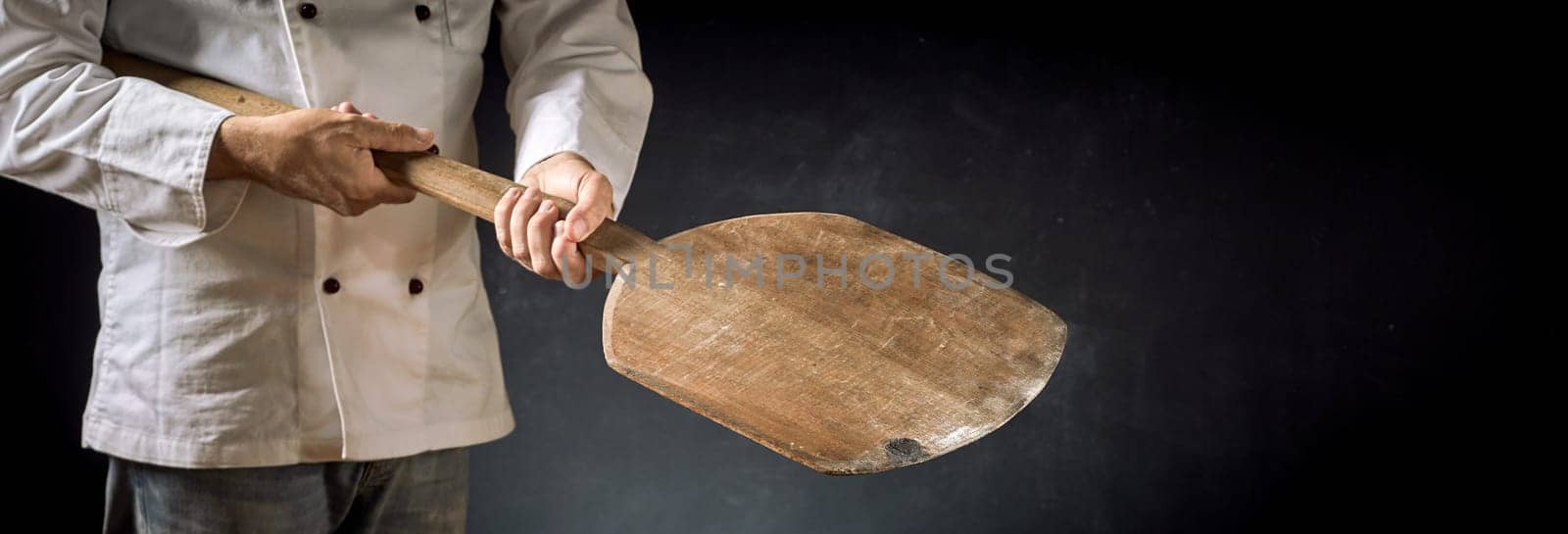 Cook or chef in a pizzeria holding an empty wooden paddle in a close up on his hands over a dark background with copy space for food placement