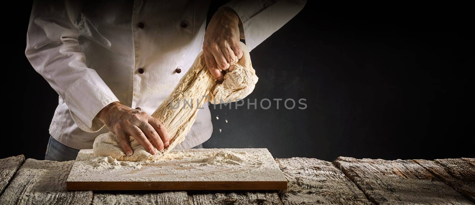 Baker or chef stretching a portion of raw dough as he works on it during preparation for cooking in a rustic panorama banner with copy space