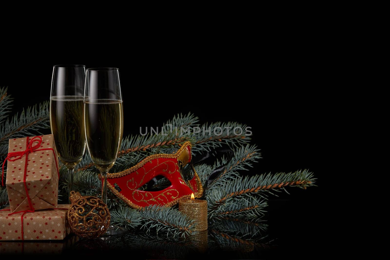 Still life with two wineglasses with champagne, gift boxes, fir tree branches and Christmas decorations on a black background. Copy space. New Year and Christmas