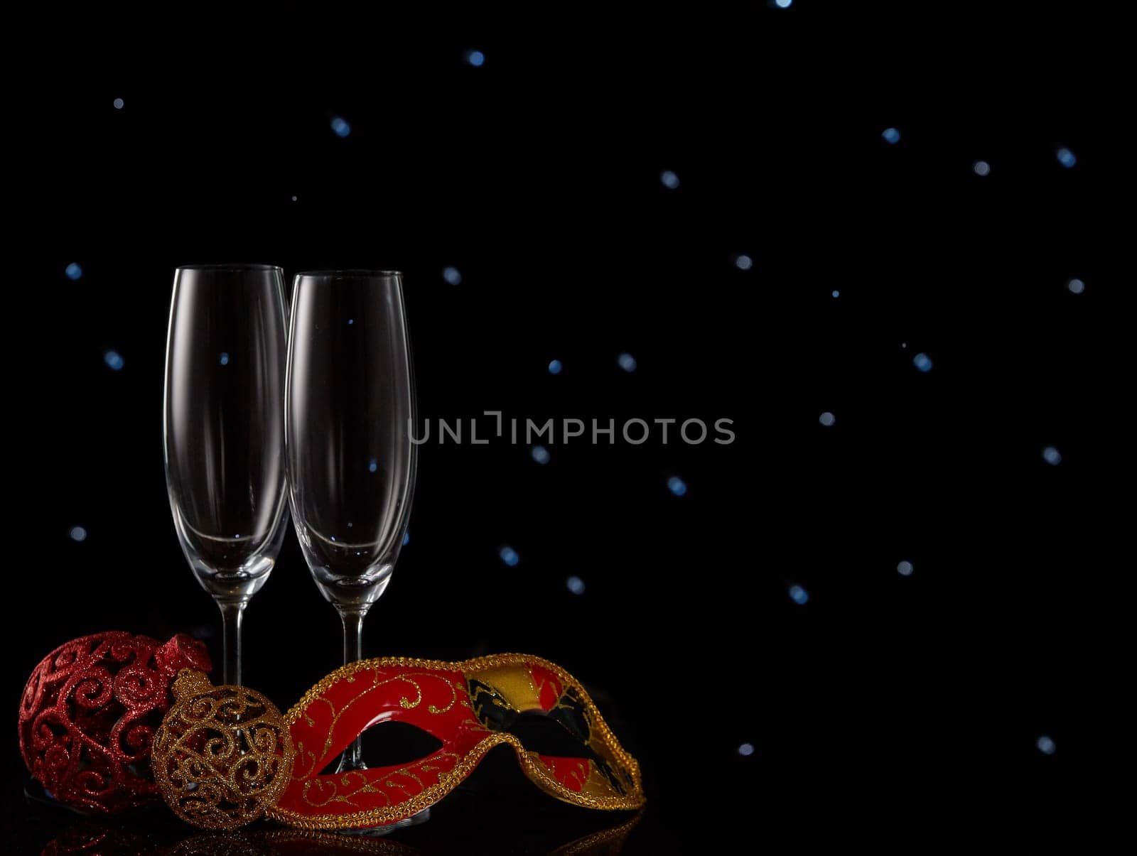 Two empty champagne flutes and Christmas decorations on a black background with LED lights garland. Copy space. New Year and Christmas