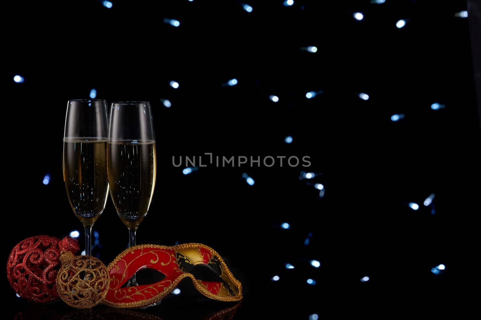 Two wineglasses with champagne and Christmas decorations on a black background with LED lights garland. Copy space. New Year and Christmas
