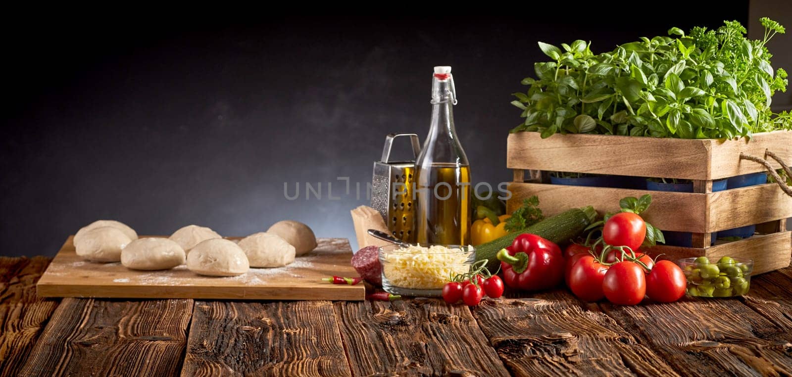 Panorama banner with fresh food ingredients for Italian cuisine including tomatoes, basil, olive oil, cheese, sweet peppers and portion of raw dough on a rustic table with copy space