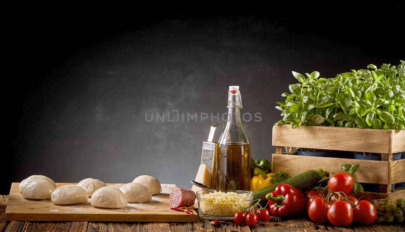 Fresh organic ingredients for an Italian pizza with individual portions of uncooked dough, basil, tomatoes, cheese, sweet peppers and olive oil over a dark background with copy space