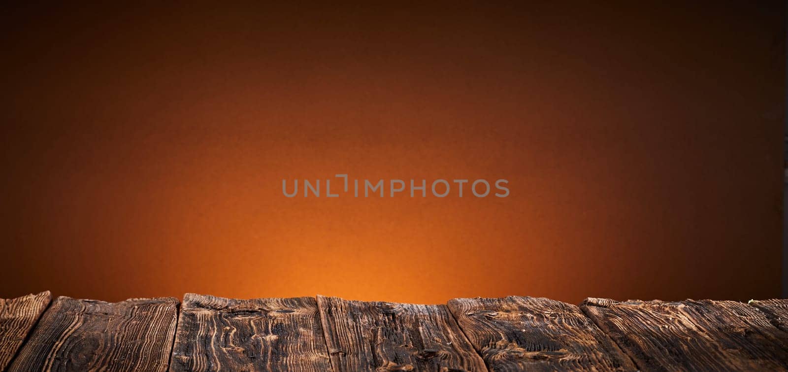 Rustic empty bare vintage wood table background over a brown background with copy space in a wide angle panorama with glow of a fire behind
