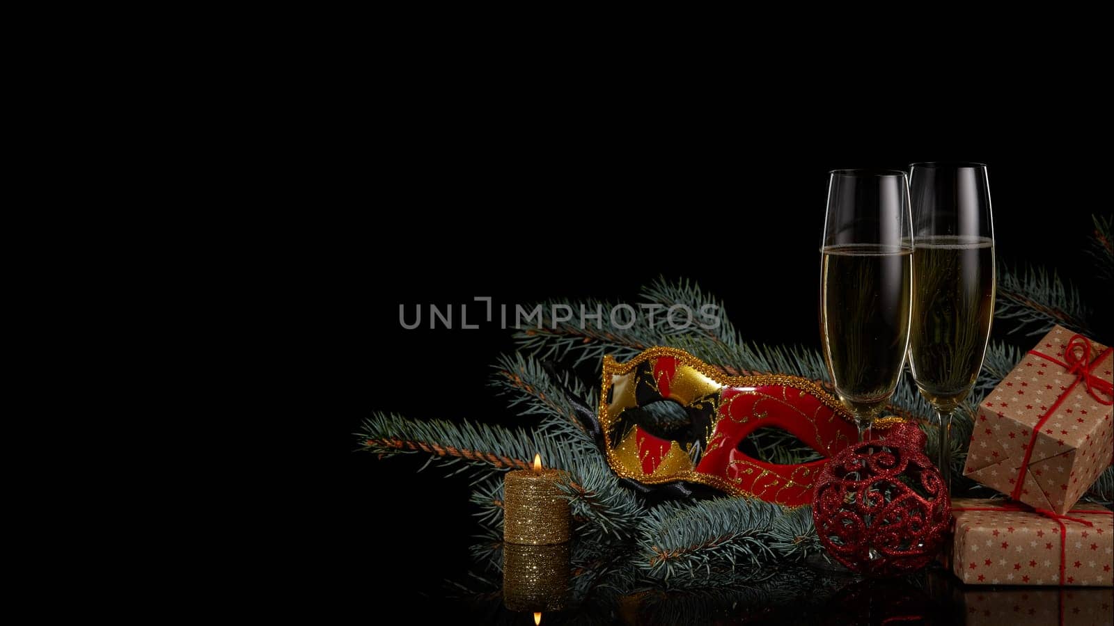 Still life with two wineglasses with champagne, gift boxes, fir tree branches and Christmas decorations on a black background. Copy space. New Year and Christmas