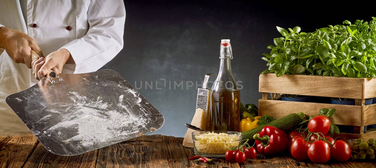 Chef holding a metal paddle with flour ready for making a traditional Italian pizza with ingredients on a rustic table in a panorama banner