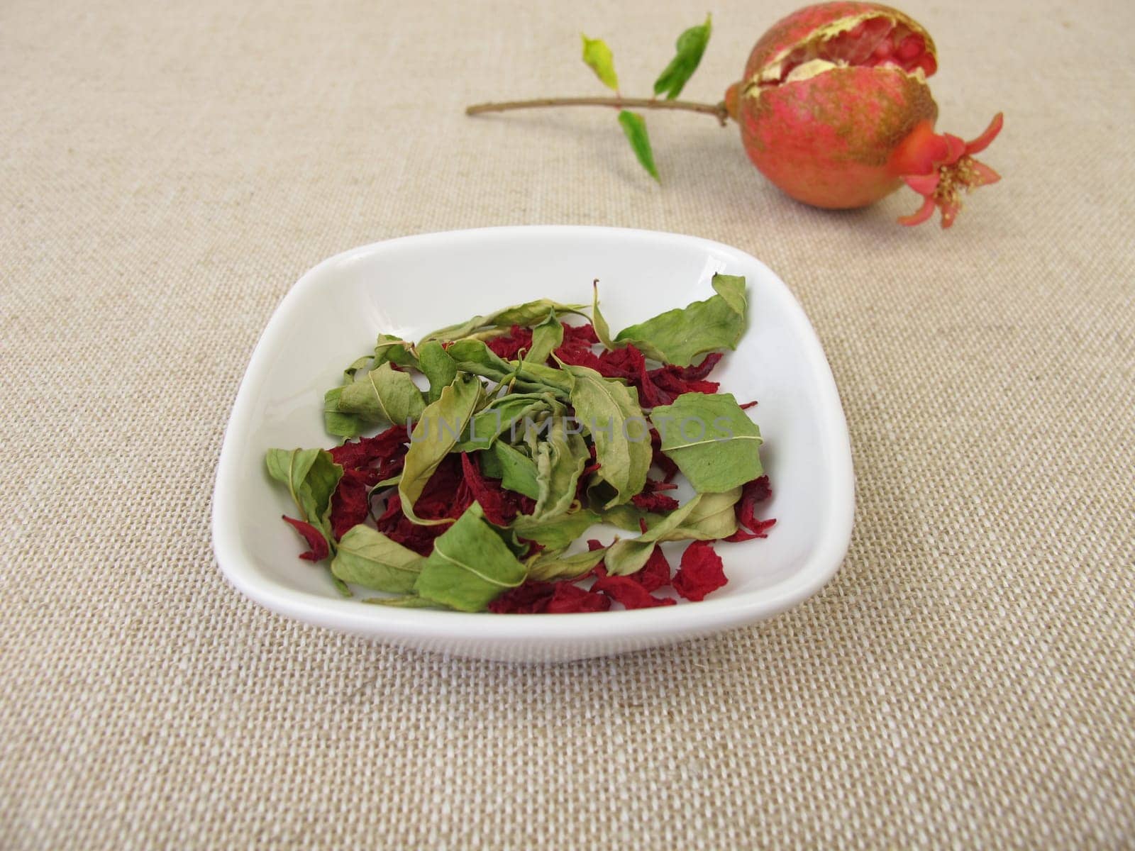 A small pomegranate, pomegranate leaves and pomegranate blossoms in a bowl