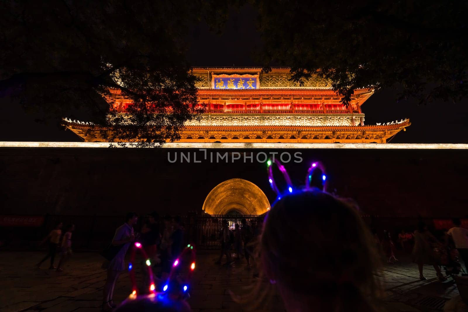 Xian, China -  July 2019 : Children with lighting LED ears accesory on their heads standing in front of the Xian Bell Drum Tower beautifully lit and illuminated at night, Shaaxi Province