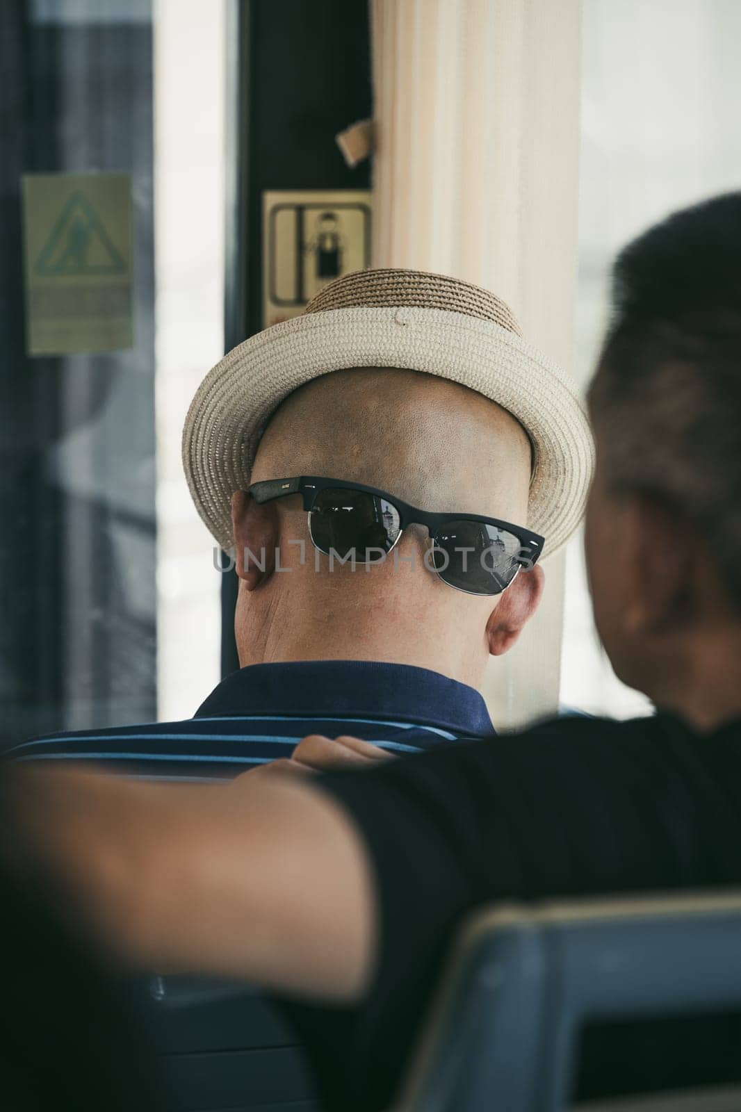 Xian, China -  July 2019 : A chinese man wearing his sunglasses on the back of his shaved head with a hat that gives the illusion of a face, public transport
