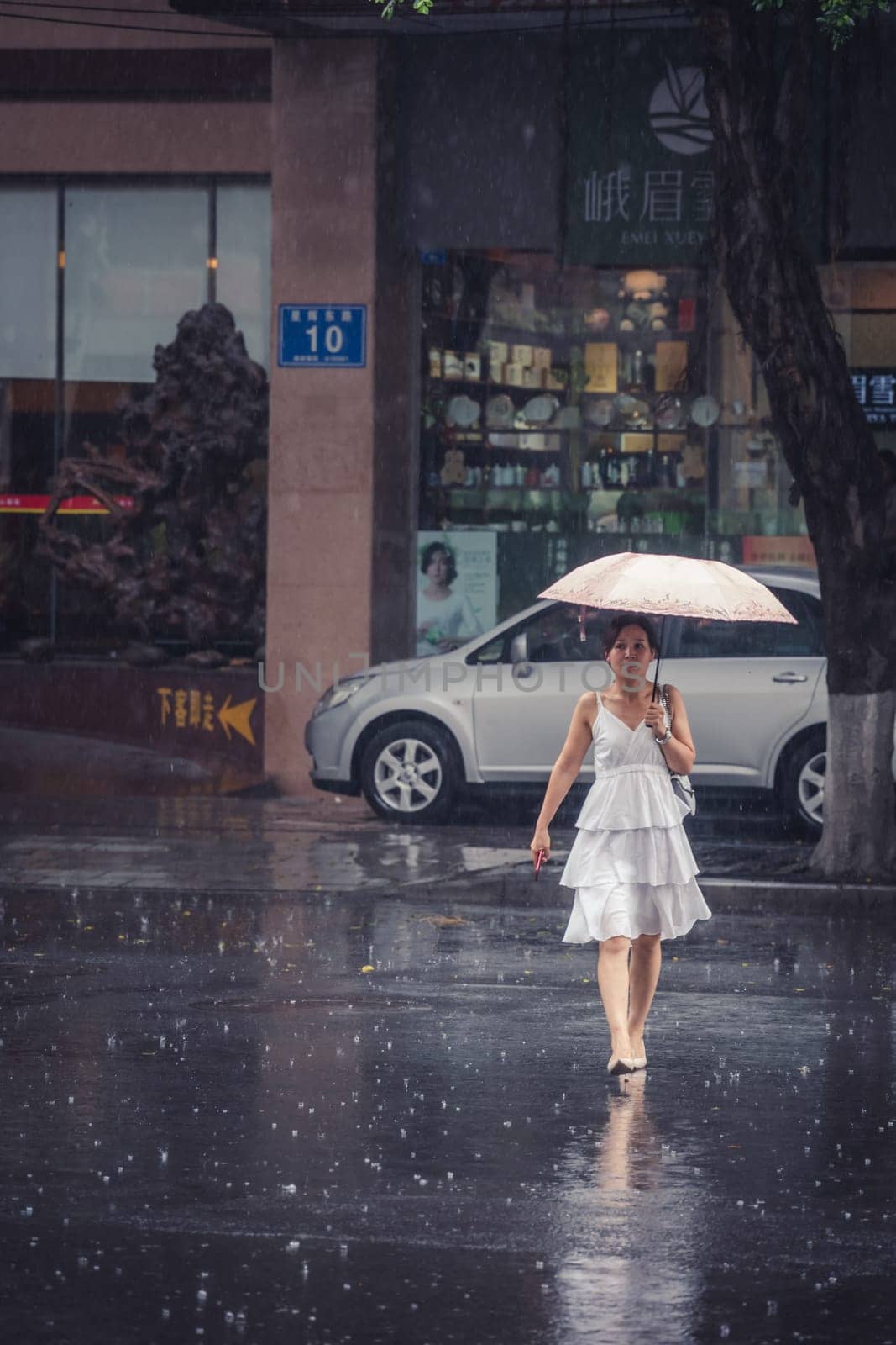 Chengdu, China -  July 2019 : Beautiful Chinese woman in a bridal white dress walking with an umbrella during tropical monsoon rain
