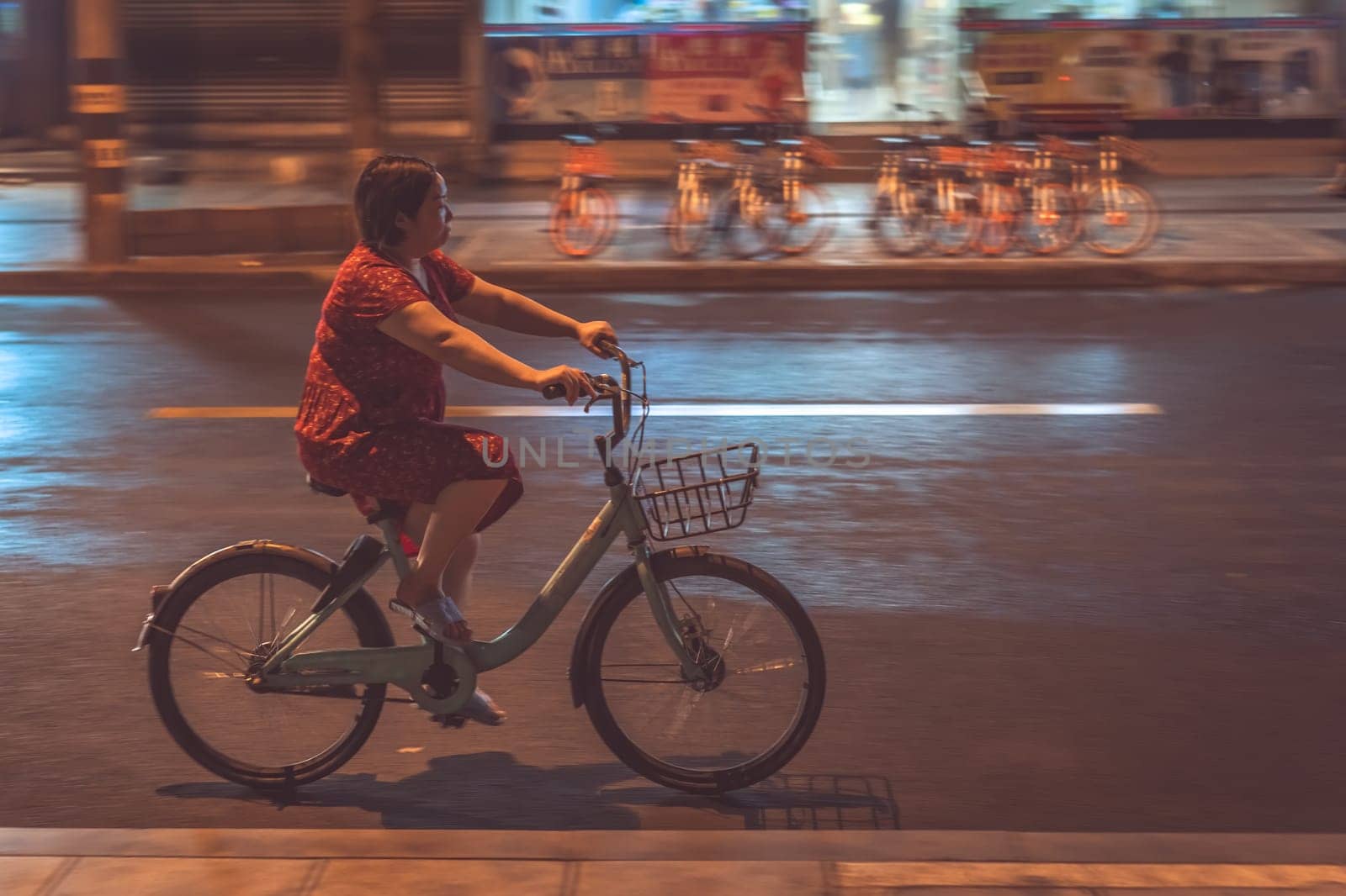 Chengdu, China -  July 2019 : Chinese woman cycling on a bicycle at night on a street