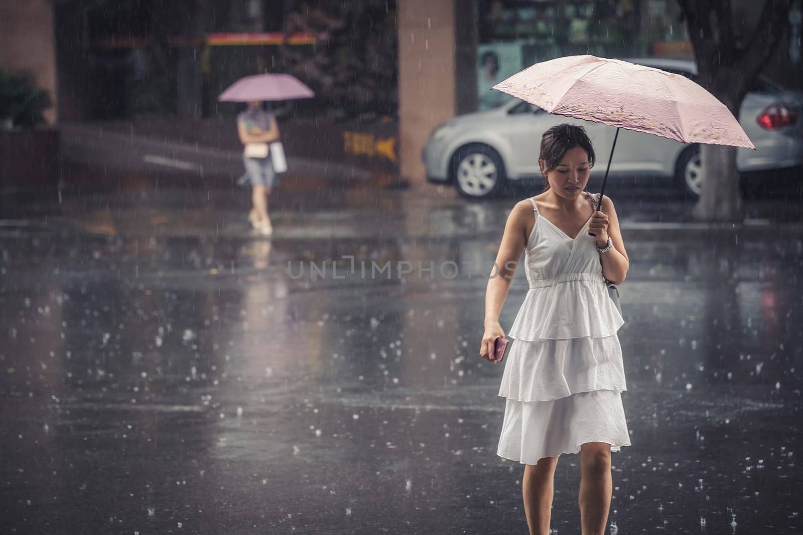 Chengdu, China -  July 2019 : Beautiful Chinese woman in a bridal white dress walking with an umbrella during tropical monsoon rain