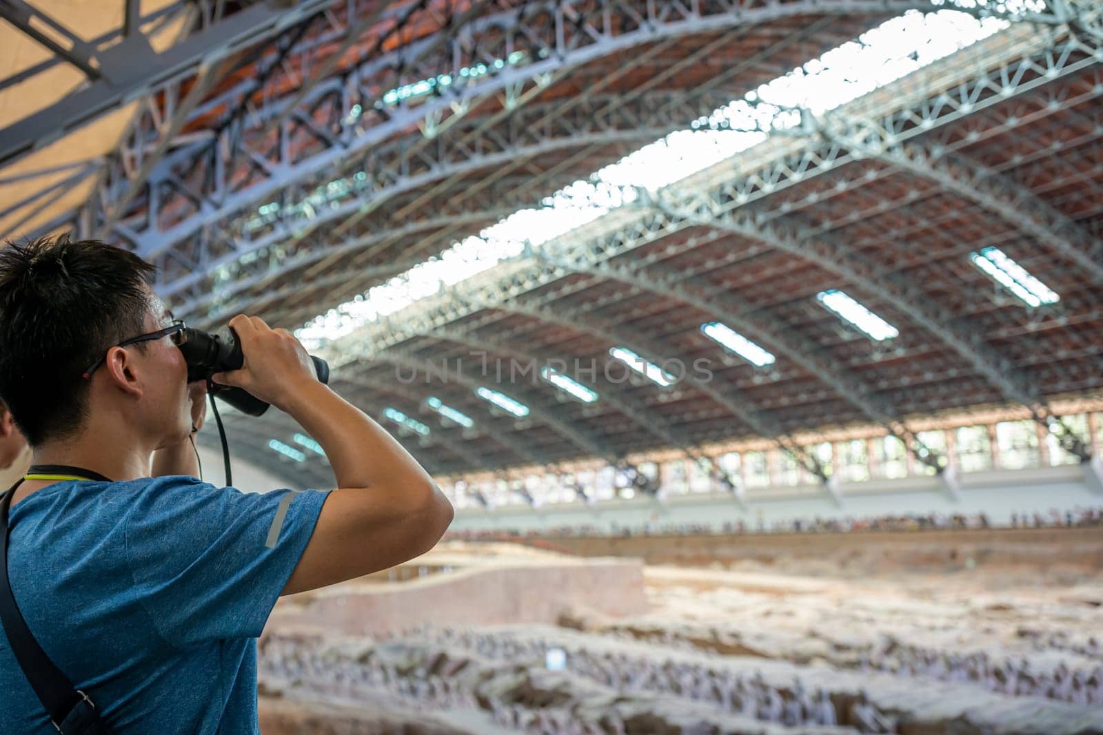 Xian, China -  July 2019 : Chinese tourist looking through the binoculars at the Terracota Army, Xian, Shaanxi Province