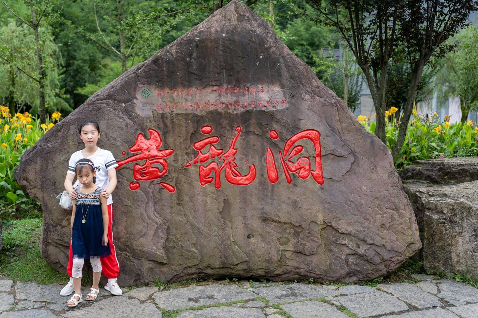 Wullingyuan, China -  August 2019 : Children posing for a picture in front of a large boulder with chinese characters written in red on it,  Hunan Province