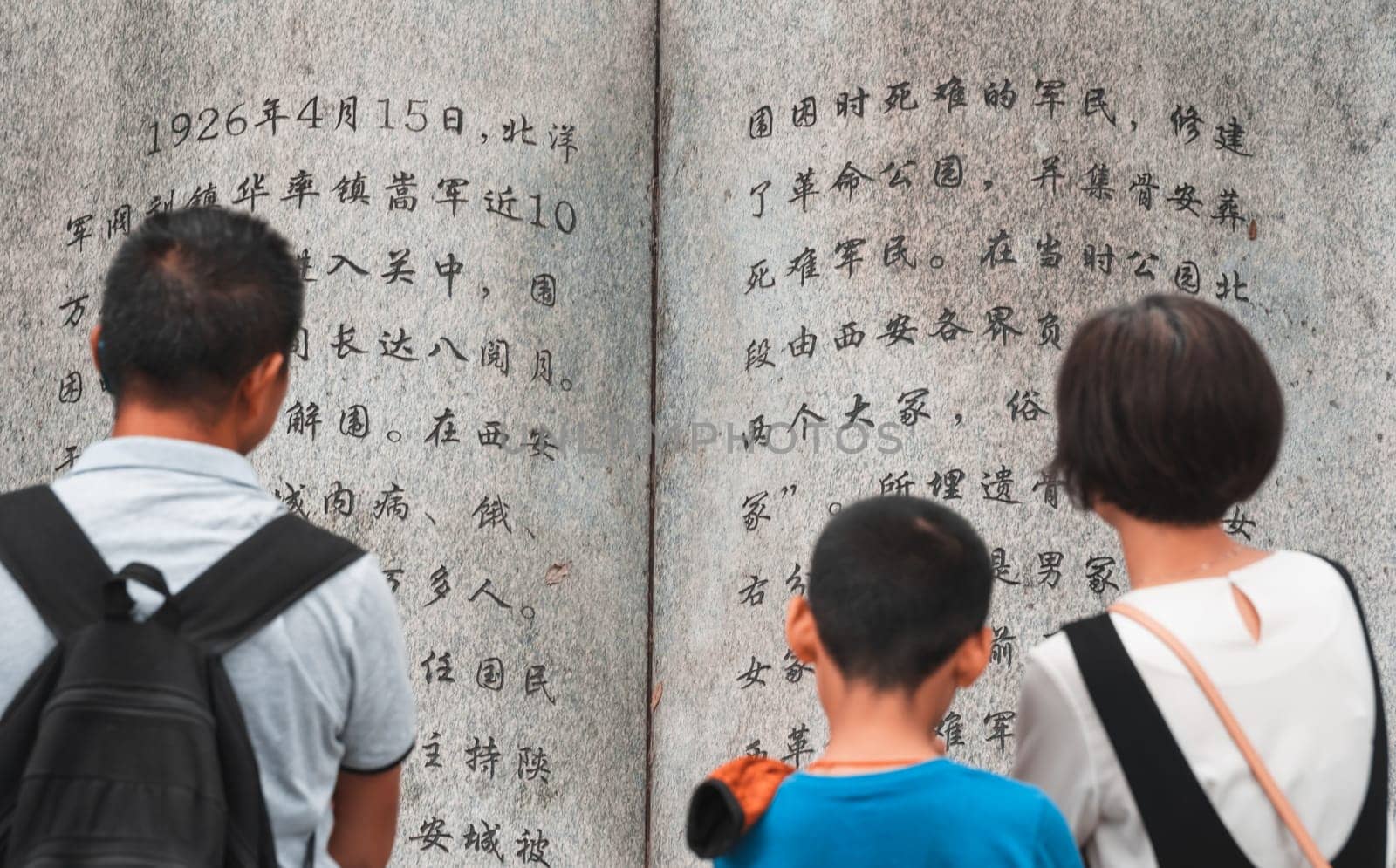 Xian, China -  August 2019 : Family reading text from a page in a large sculpture stone book in Geming Revolution Park, Shaanxi Province