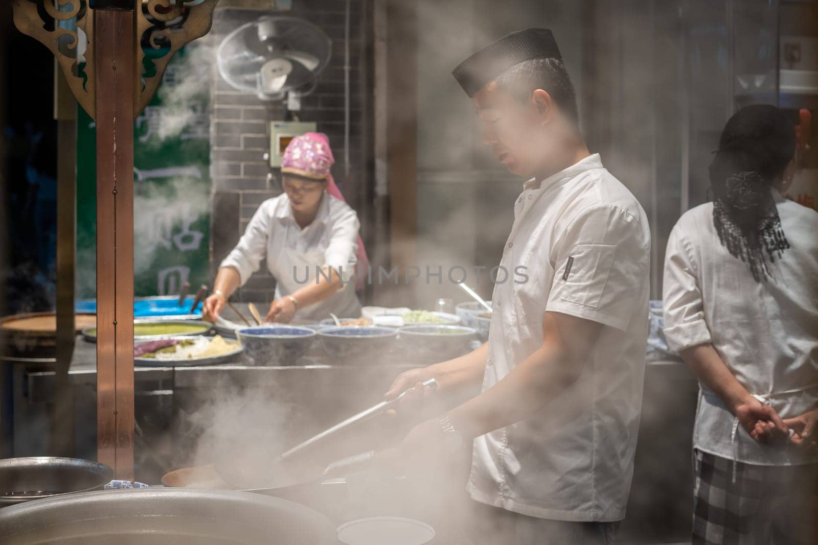 Xian, China -  August 2019 : Chinese chef preparing hot food on a food stall operating at night on the street in the Muslim Quarter