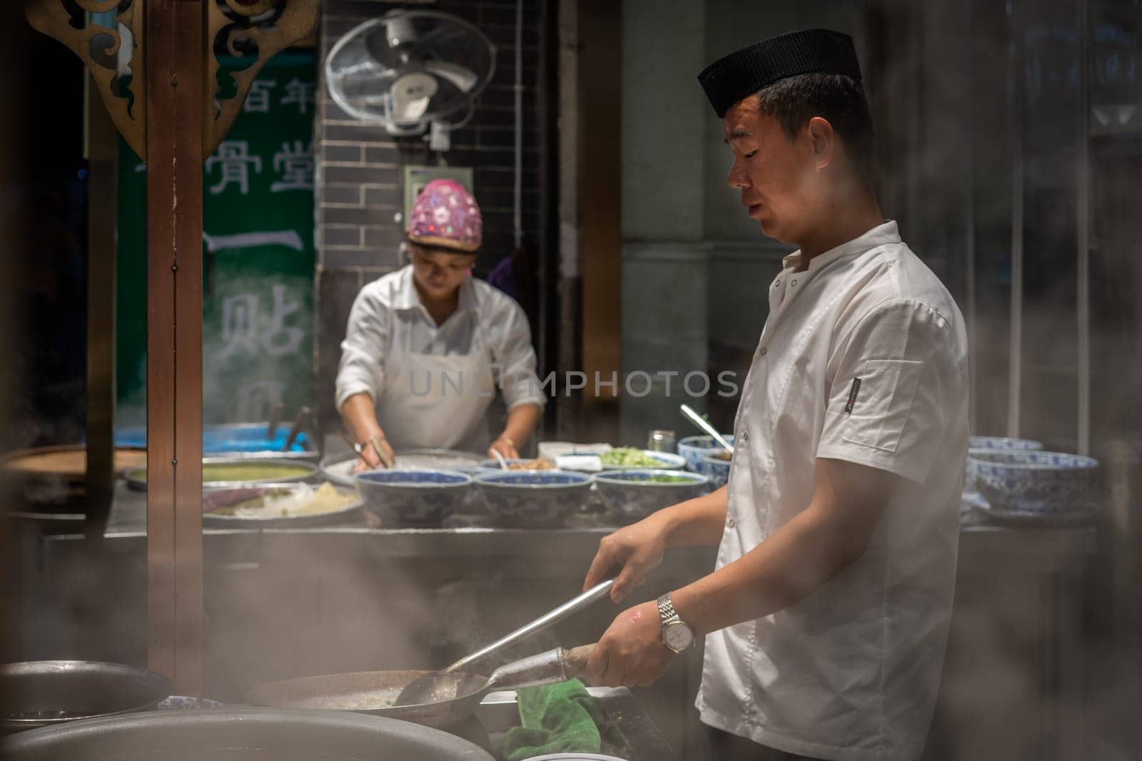 Xian, China -  August 2019 :  Chinese chef preparing hot food on a food stall operating at night on the street in the Muslim Quarter