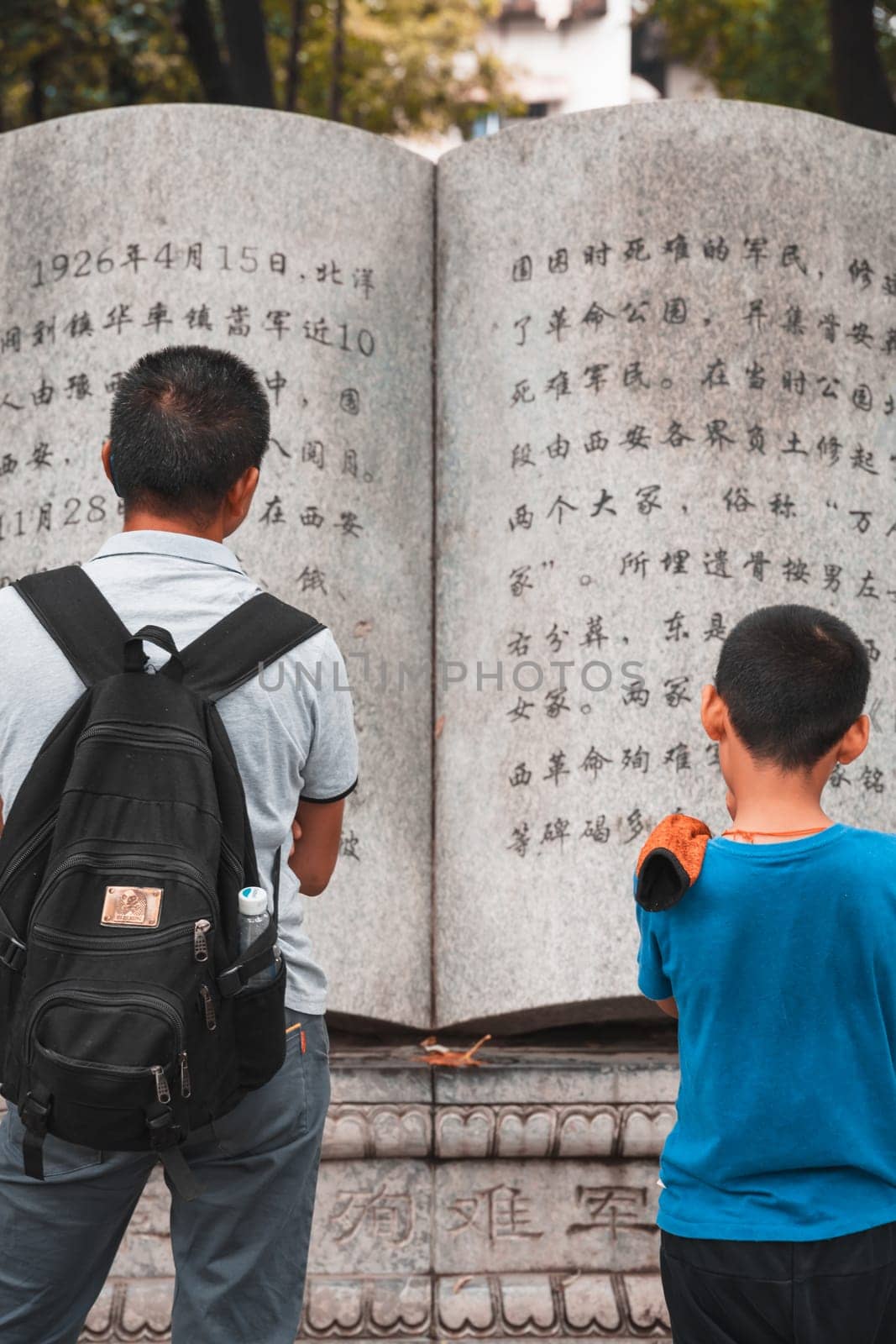 Xian, China -  August 2019 : Father and son reading text from a page in a large sculpture stone book in Geming Revolution Park, Shaanxi Province