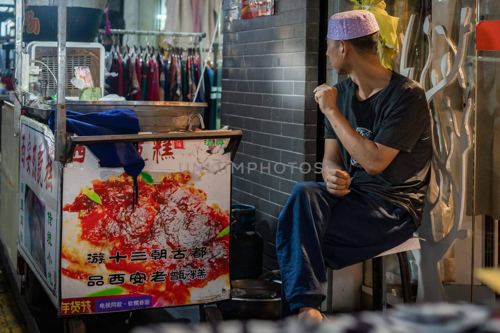 Xian, China -  August 2019 :  Bored seller sitting on a chair on a stall in Muslim Quarter in Xian town, Shaanxi Province