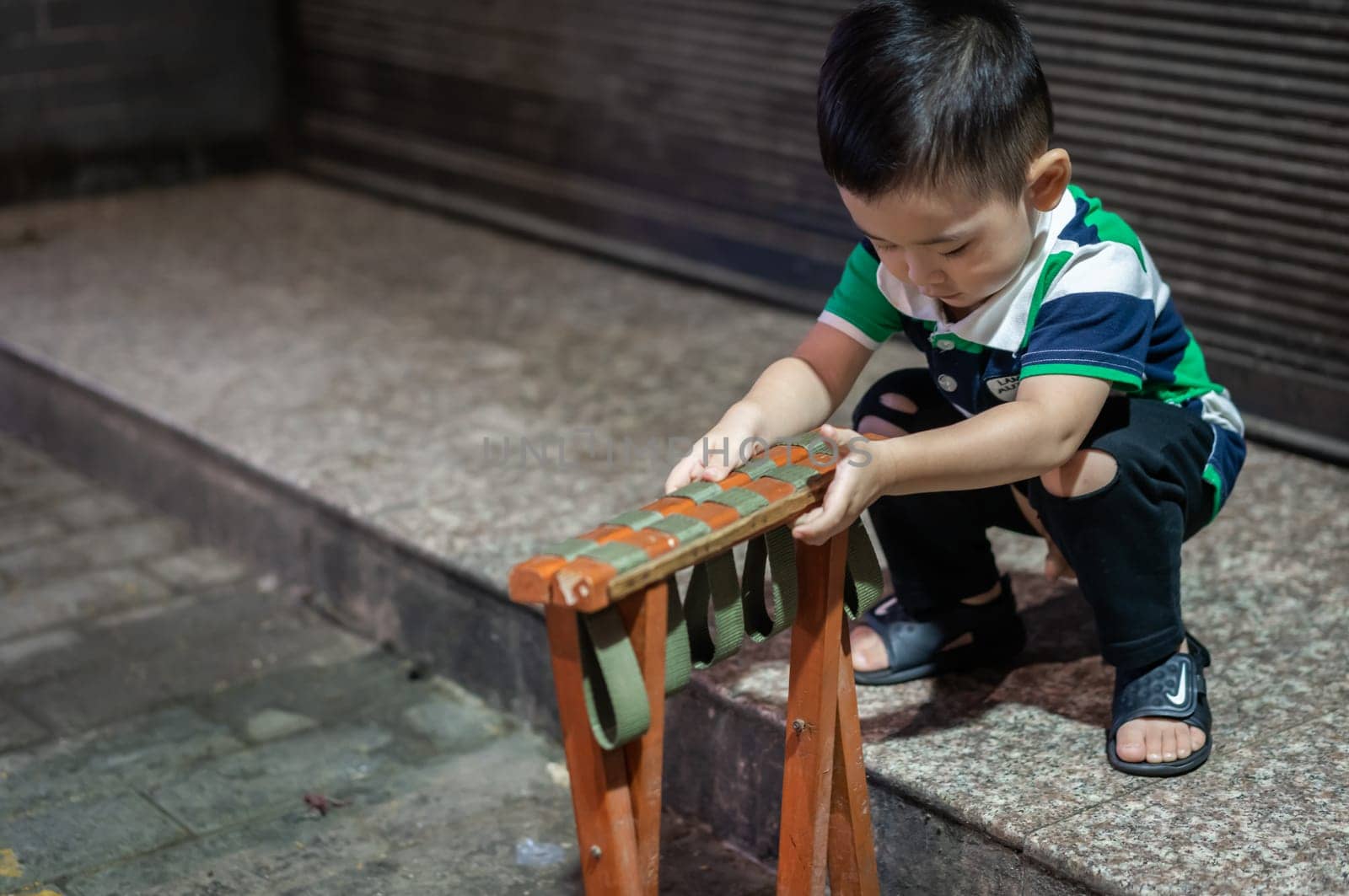 Xian, China -  August 2019 : Cute little chinese boy playing with folding chair outside small local bakery on the street in Muslim Quarter