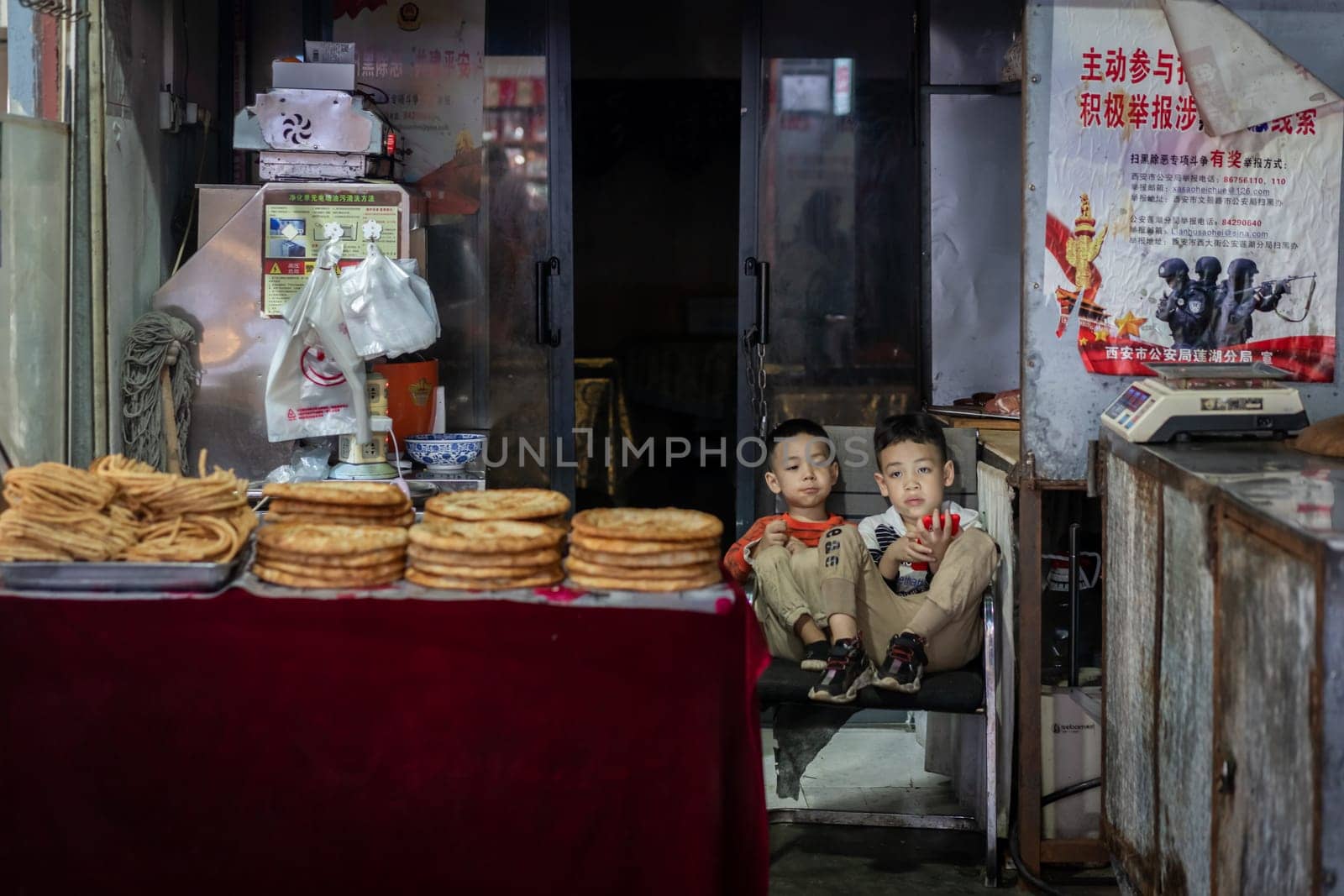 Xian, China -  August 2019 :  Two little boys playing games on a small mobile device while sitting on chairs in a small local bakery on the street in Muslim Quarter