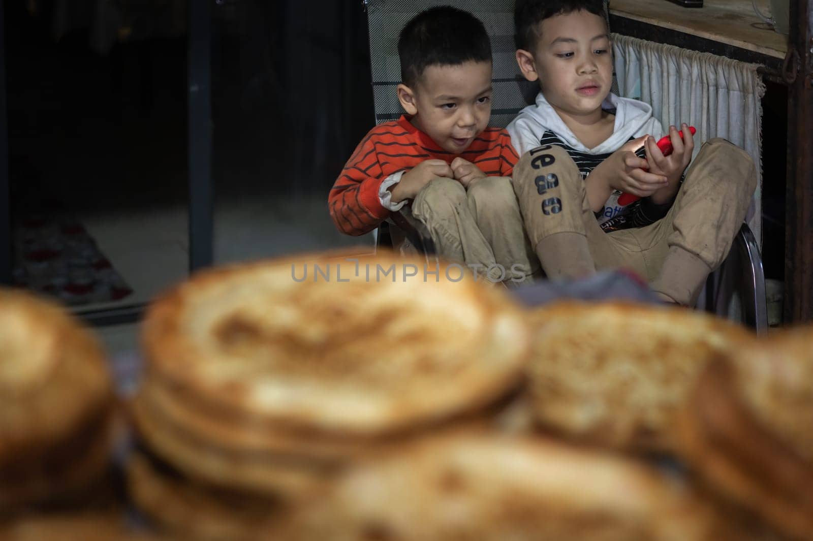 Xian, China -  August 2019 :  Two little boys playing games on a small mobile device while sitting on chairs in a small local bakery on the street in Muslim Quarter