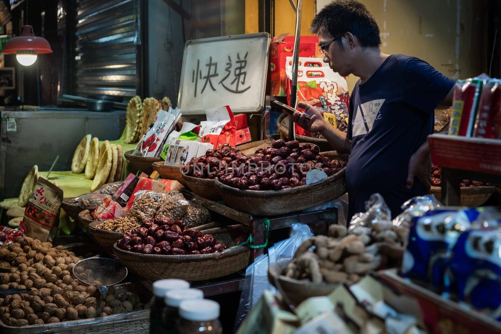 Xian, China -  August 2019 : Bored fruit seller checking his smartphone on a stall in Muslim Quarter in Xian town, Shaanxi Province