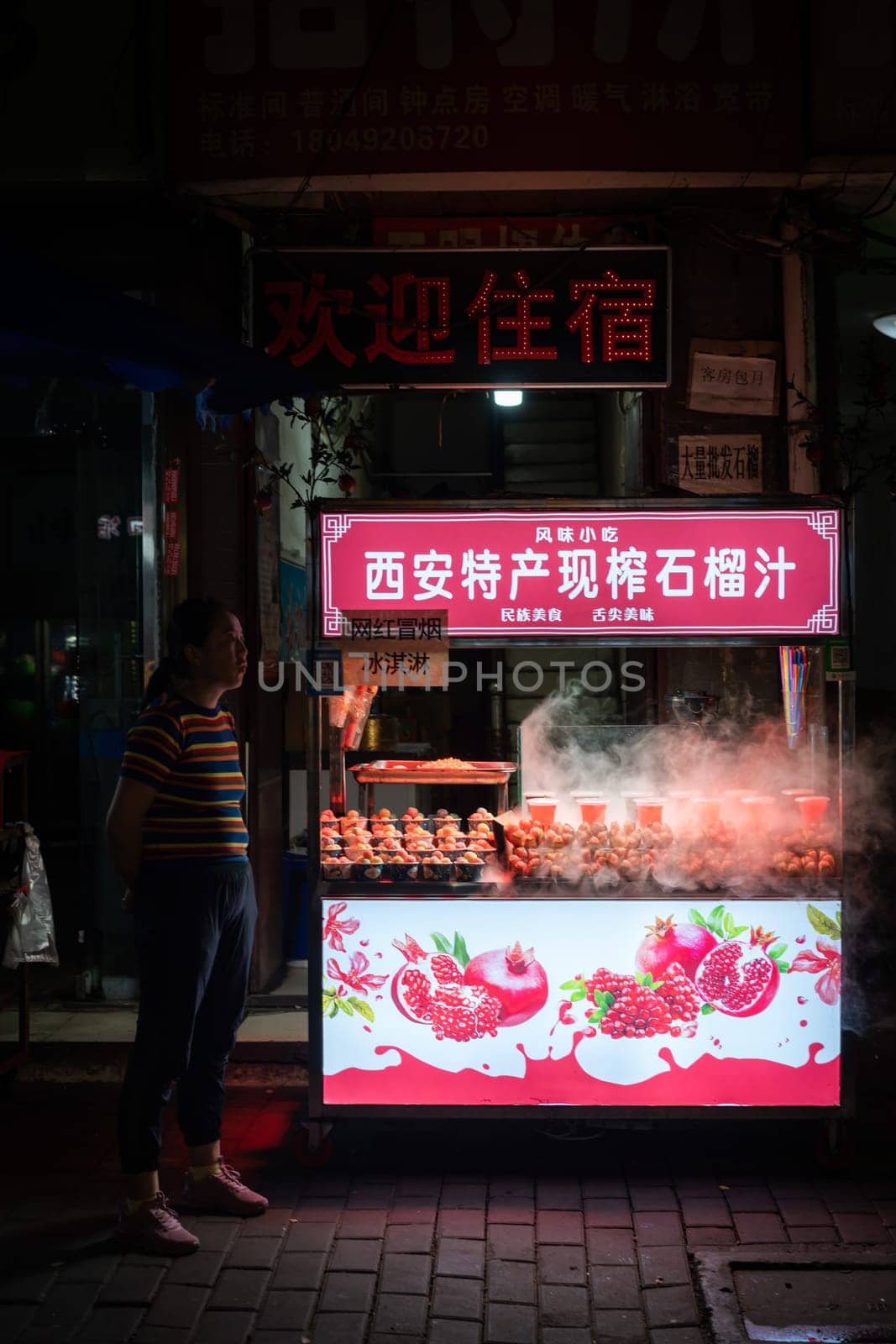 Xian, China -  August 2019 : Woman standing in front of the Fresh pomegranate juice stall operating at night on the street in the Muslim Quarter