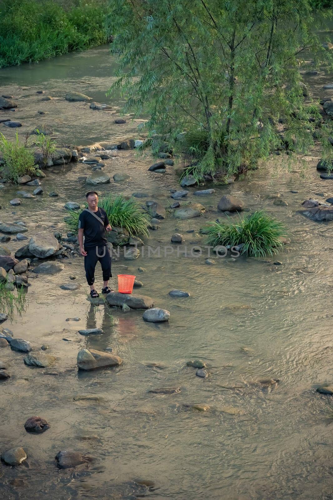 Wulingyuan, China -  August 2019 : Chinese fisherman standing in a shallow river