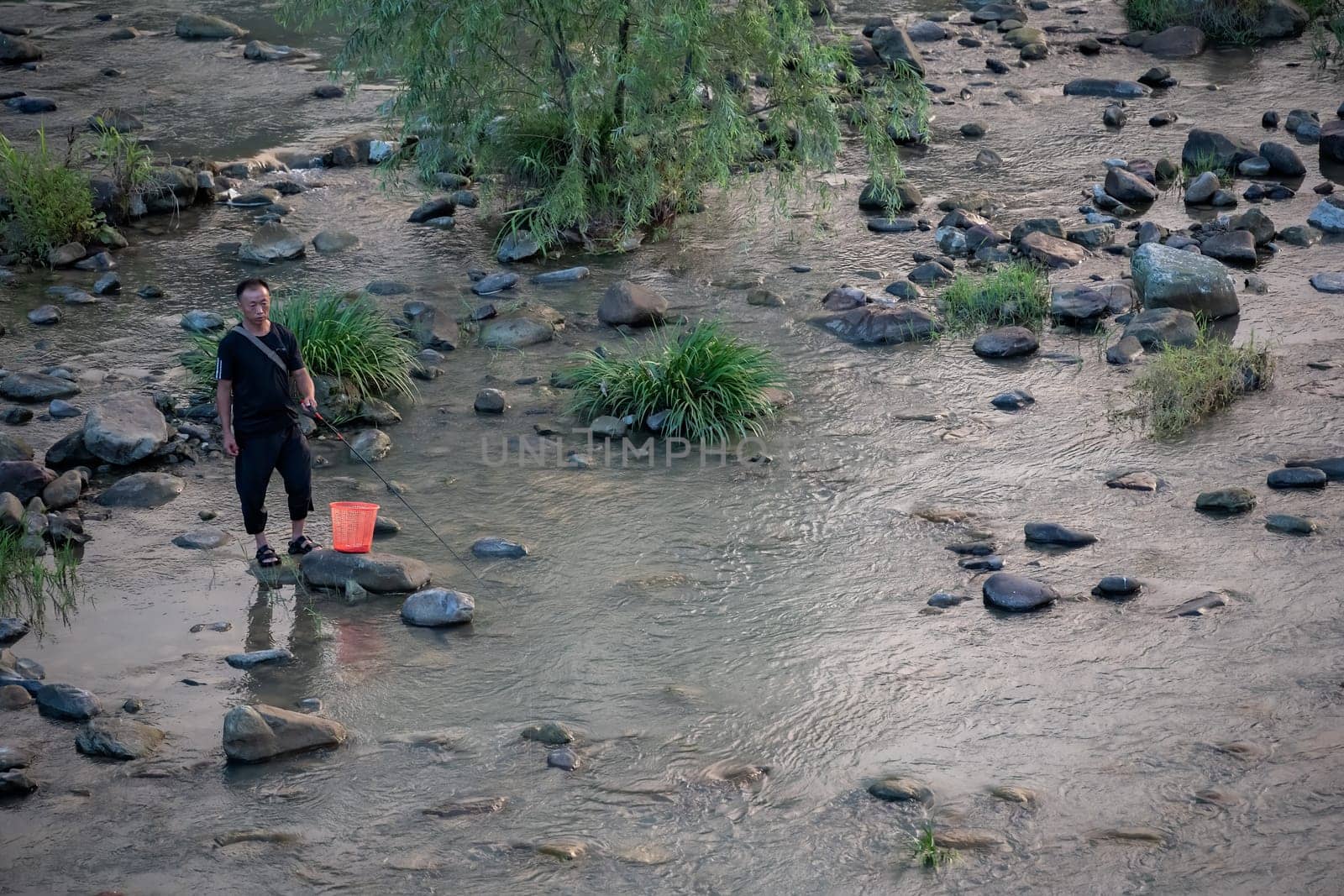 Wulingyuan, China -  August 2019 : Chinese fisherman standing in a shallow river