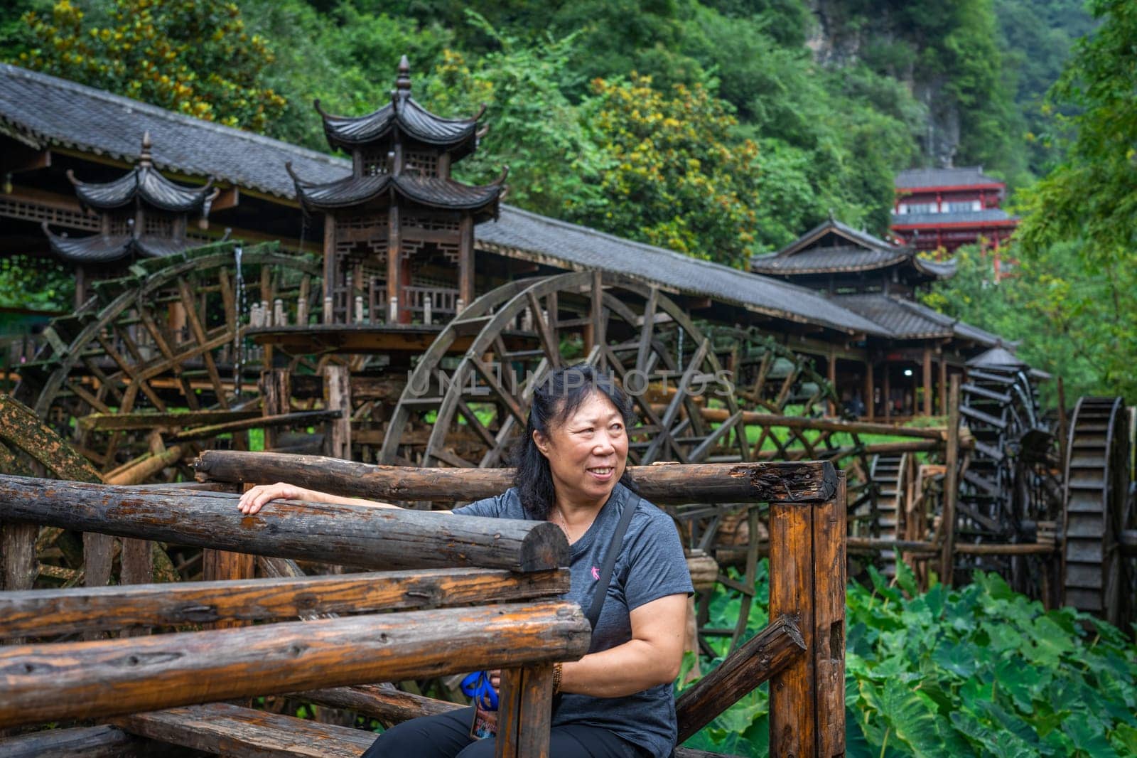 Wullingyuan, China -  July 2019 : Older chinese woman using her legs to pull levers on a wheel of an old Water wheel in Huanglong Yellow Dragon Cave scenic area, Zhangjiajie, Hunan Province
