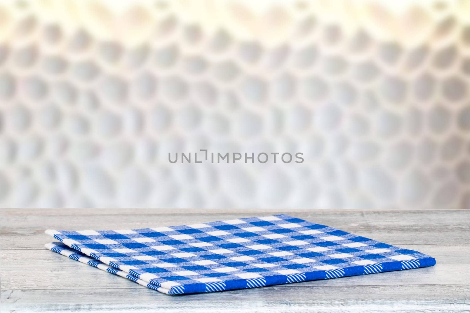 Closeup of a empty blue checkered tablecloth or napkin on a rustic bright gray table over abstract blurred  bright background. Template for food and product display montage.