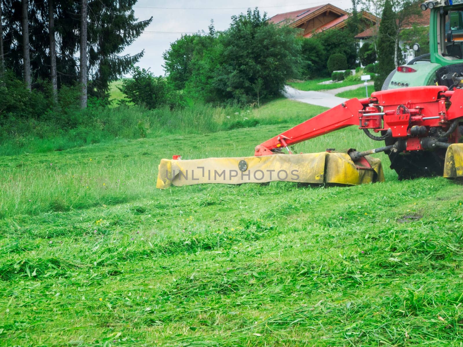 Tractor with grass cutting header at work on a hilly meadow in Bavaria.
