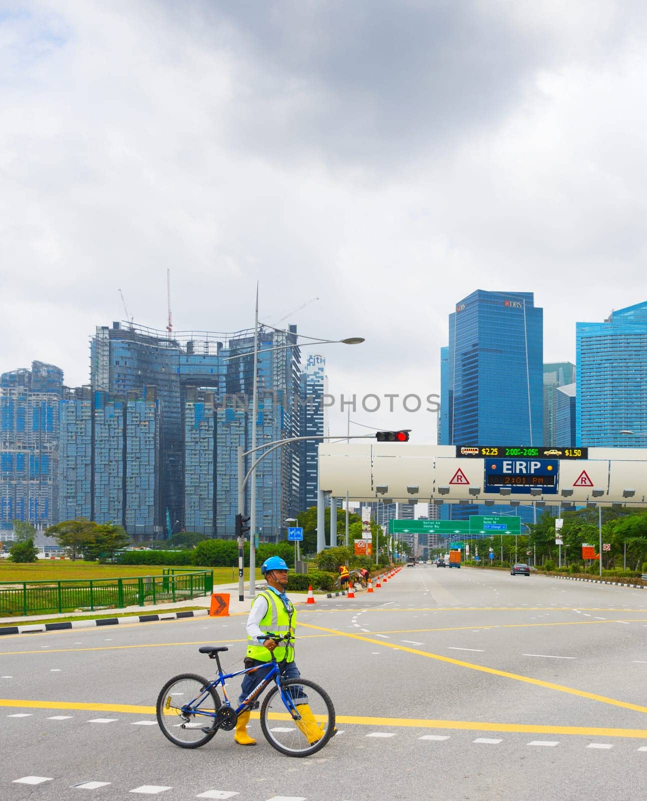SINGAPORE - FEBTUARY 16, 2017: Construction site worker in helmet and vest crossing road with bicycle, Singapore downtown skyline in background