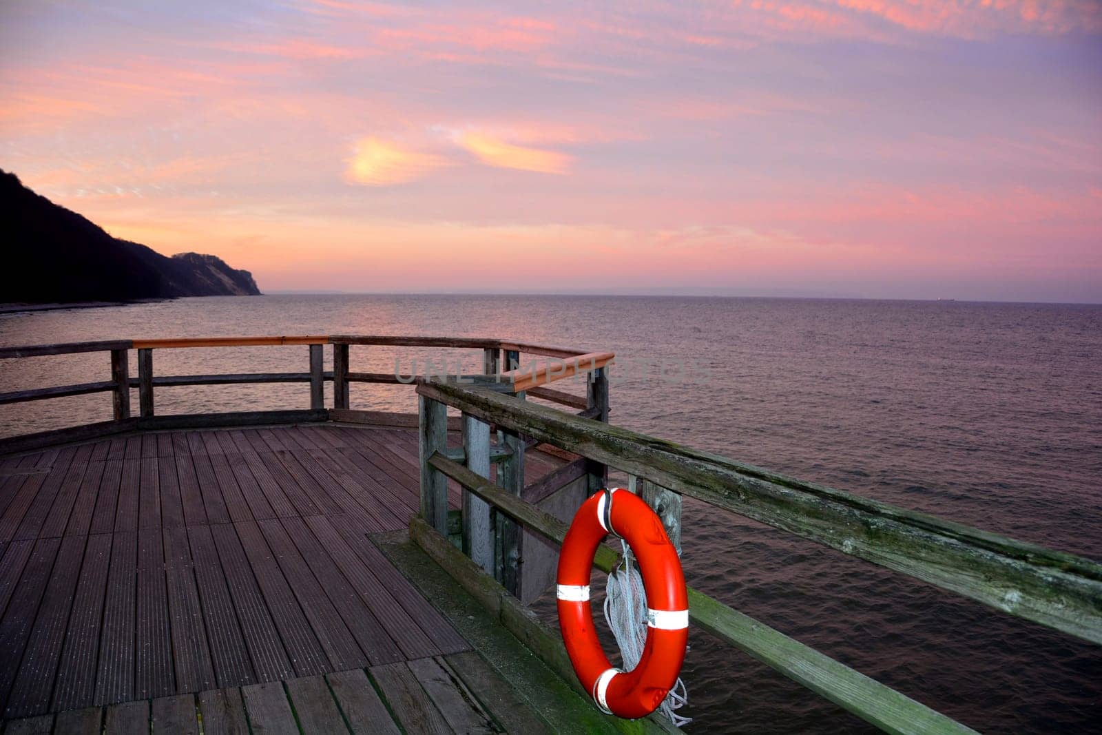 Wooden pier with a red lifebuoy on the Baltic Sea after sunset, overlooking the sea with copy space