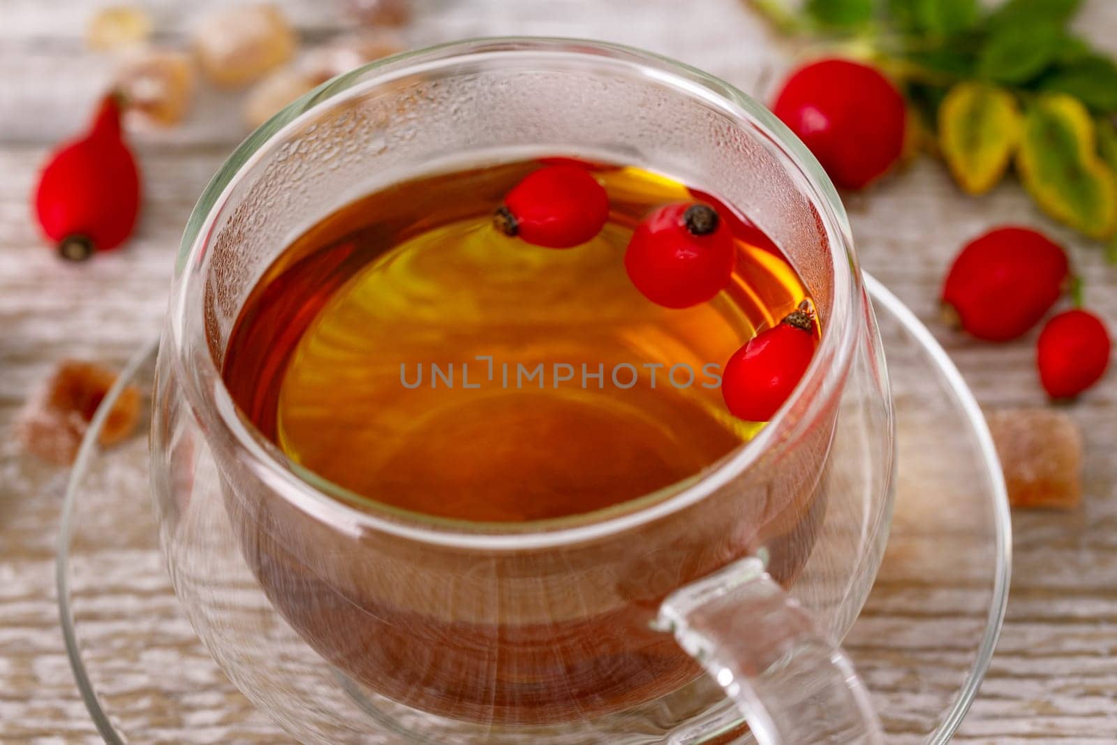 Rosehip tea in a glass cup with rose hips around the cup