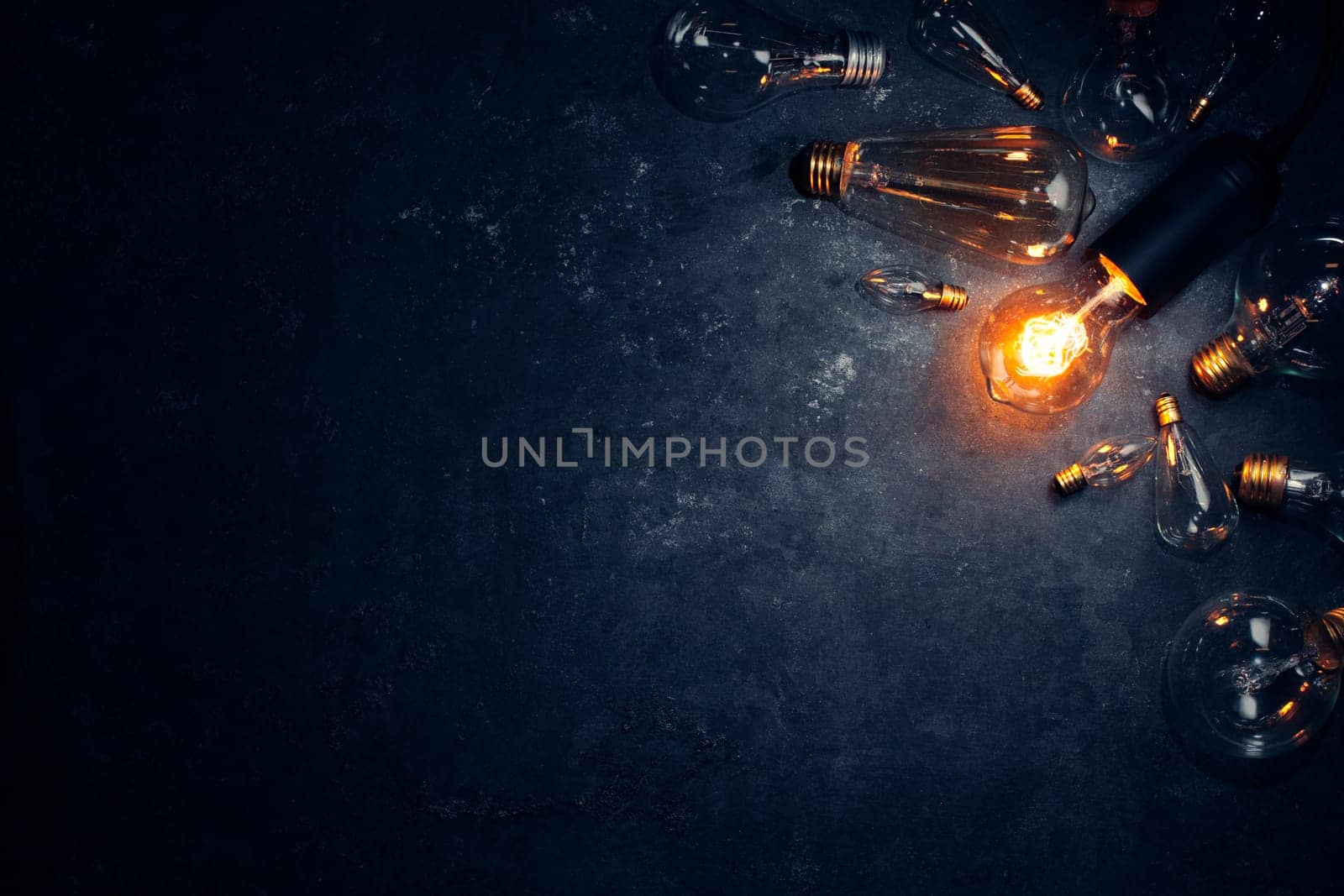 Vintage old light bulb glowing yellow on rough dark background surrounded by burnt out bulbs. Idea, creativity concept.