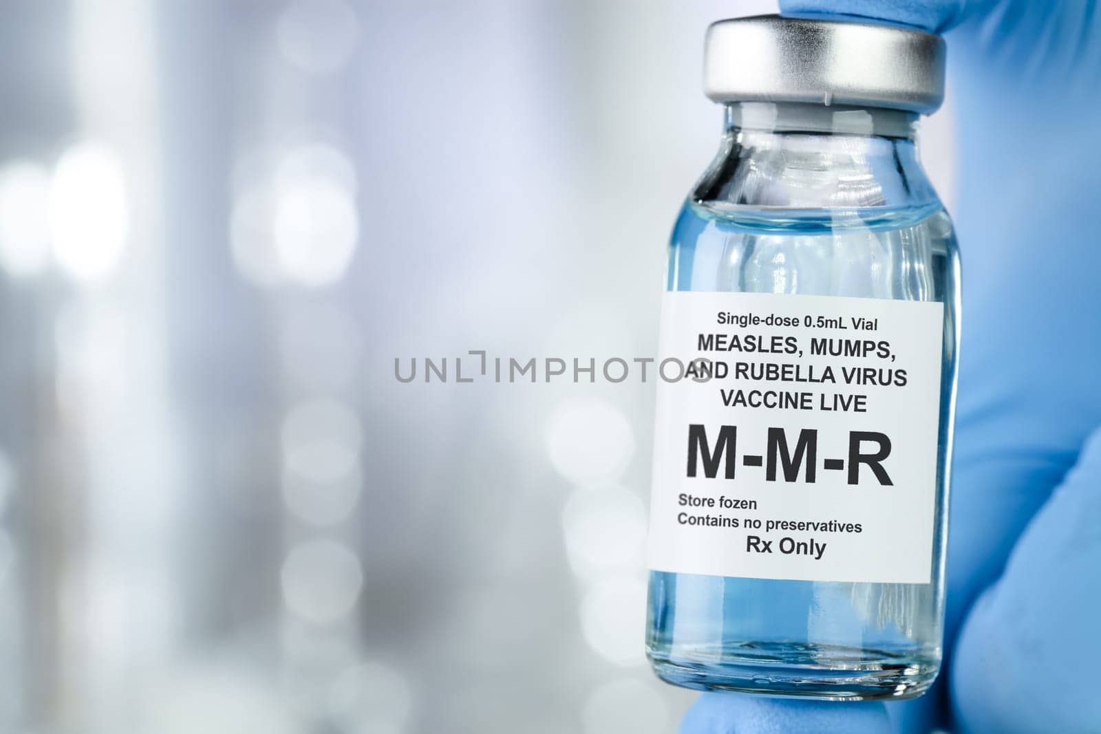 Healthcare concept with a hand in blue medical gloves holding MMR, measles, mumps, and rubella, vaccine vial