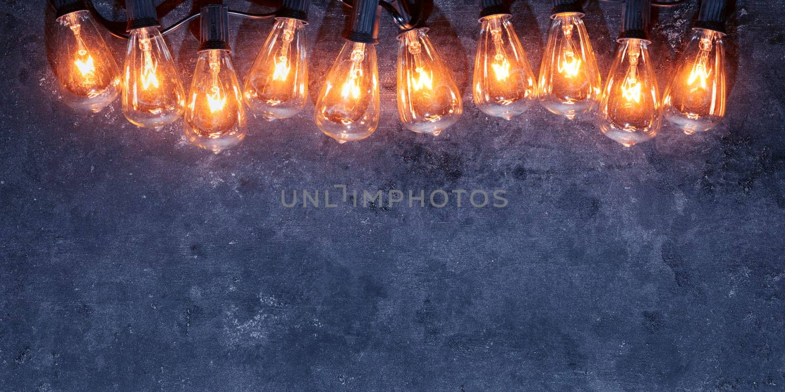 Row of lit string light bulbs glowing on dark grungy background.